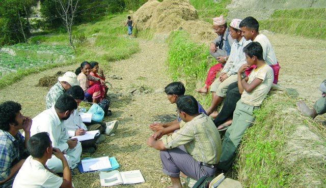 Group of people gathered outdoors, some seated, some taking notes